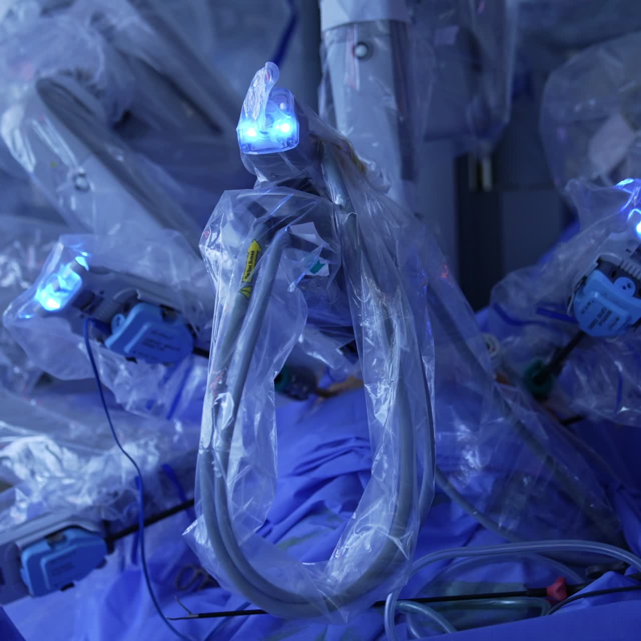 Da Vinci operating robot with arm covered in plastic for sterility. Unknown surgeon standing beside and holding an instrument