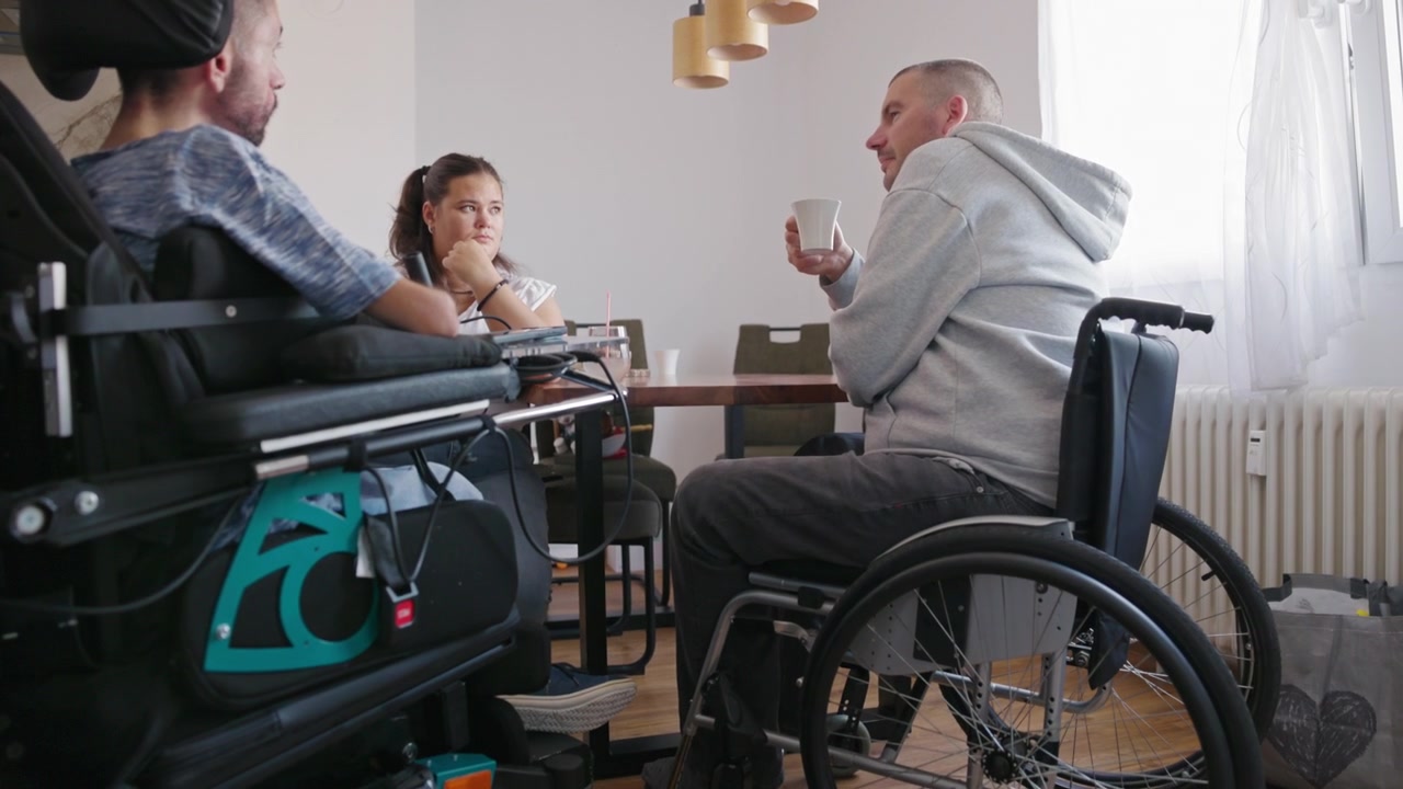 Due uomini con disabilità e un assistente di supporto che si godono il parlare insieme e la condivisione di esperienze