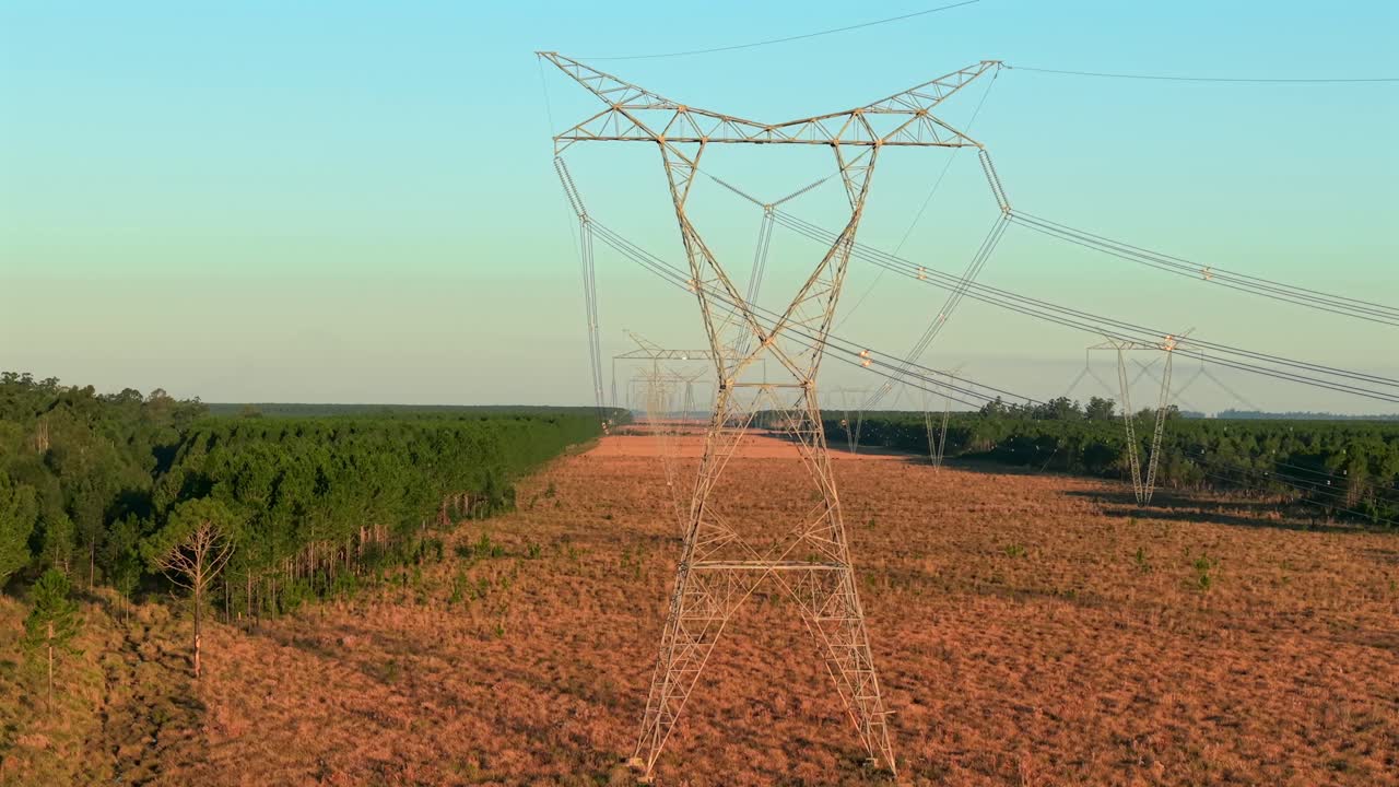 Parallel drone view of high voltage Yacireta power lines crossing over deforested terrain, Corrientes Province, Argentina