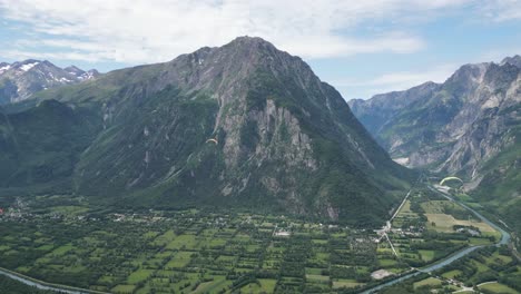 Paragliders-floating-above-Eau-d'Olle-valley-in-Alpe-d'-Huez,-French-Alps---Pan-Left