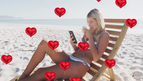 animation of heart digital icons over woman in deckchair using smartphone on beach