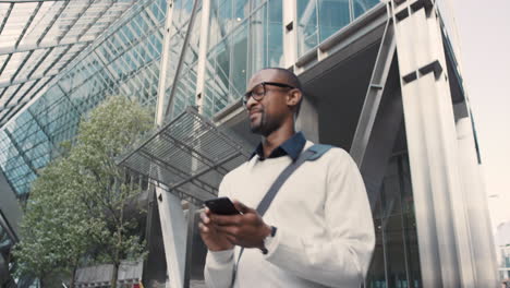 african american businessman walking through city using smart phone