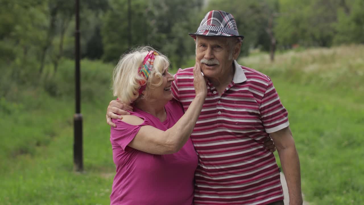 Senior caucasian couple walking in park embracing. Elderly man walks with woman. Husband, wife