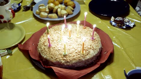 - un primer plano de velas encendidas en el pastel, que se encuentra en un plato con una servilleta roja en un mantel amarillo.