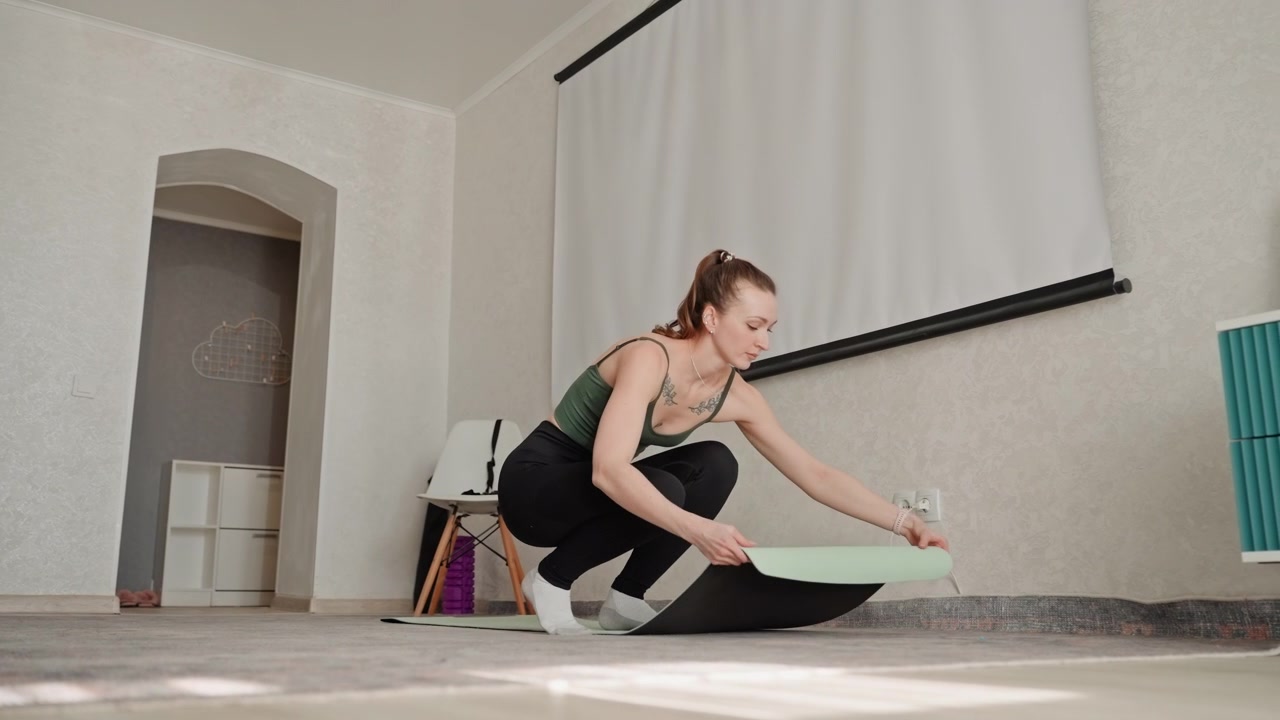 Woman sets yoga mat. Preparing space for morning yoga. Woman arranges props before starting daily exercise routine. Calm woman prepares her yoga space with props in bright room for exercise