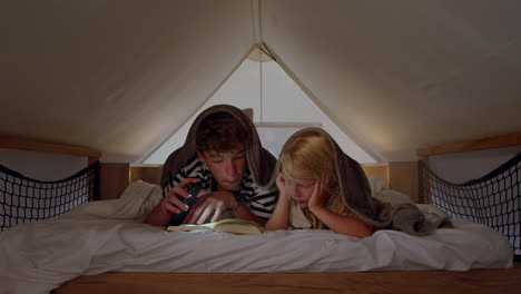 brother and sister reading a book together in a tent at night