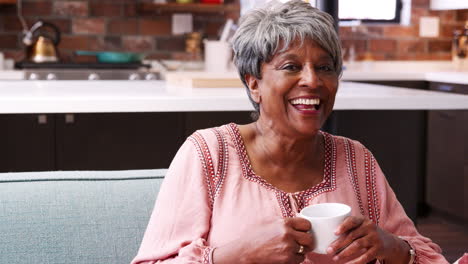 portrait of smiling senior woman relaxing with hot drink on sofa at home