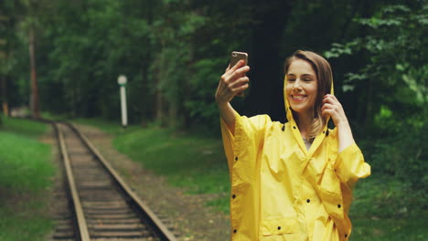 Linda-Mujer-Con-Un-Impermeable-Amarillo-Tomando-Fotos-Selfie-En-Un-Smartphone-Y-Posando