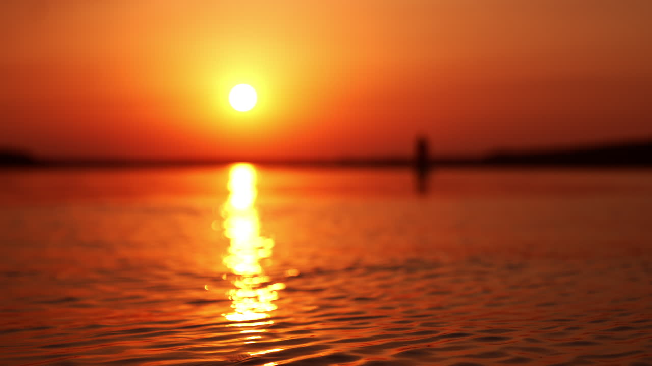 Blurred view of a river at orange sunset time. Sun reflecting on the water surface.