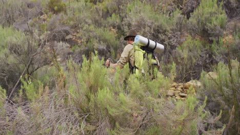 caucasian male survivalist trekking through wilderness with backpack and walking poles