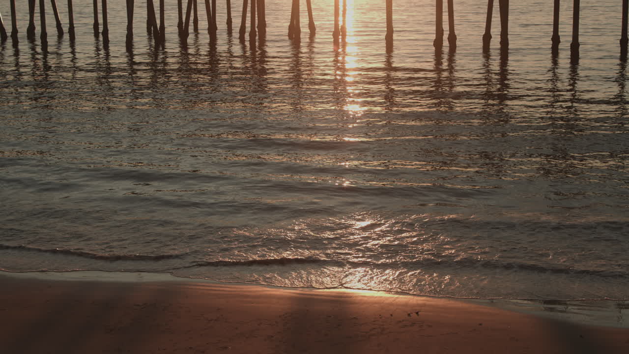 Filmato cinematografico 4K della struttura inferiore del molo di Redondo Beach senza persone, che mostra pali di legno, onde oceaniche, riflessi e una serena atmosfera costiera della California meridionale.