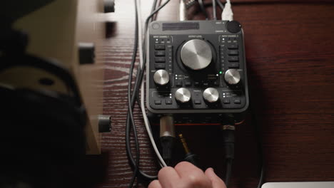 a close-up shot of a hand plugging a cable into a sound mixer, with the device powering on. the technical detail and precision involved in setting up audio equipment, with various knobs, dials