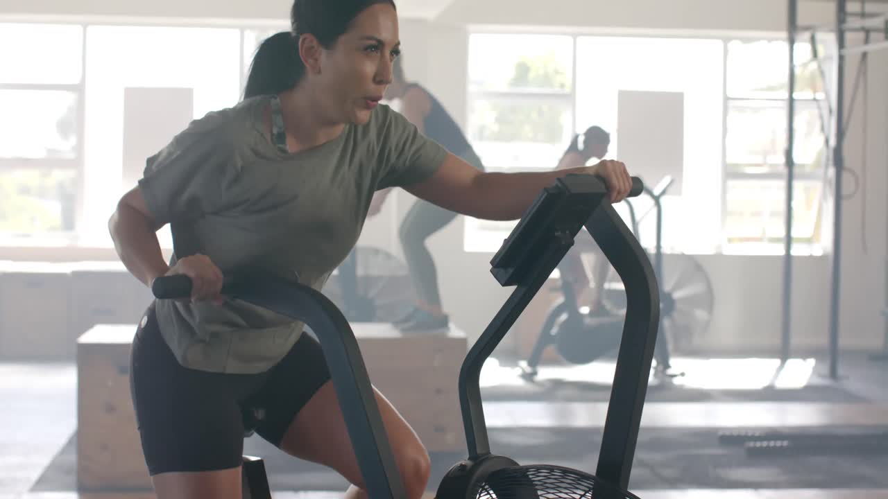 Donna caucasica determinata e naturale che si allena sulla bici ellittica in palestra, al rallentatore.