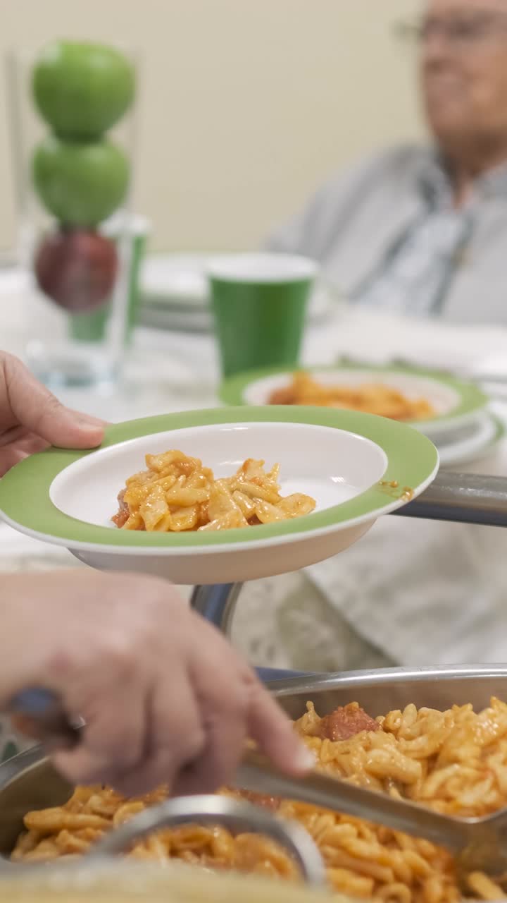 Crop worker serving pasta in plate for elderly people