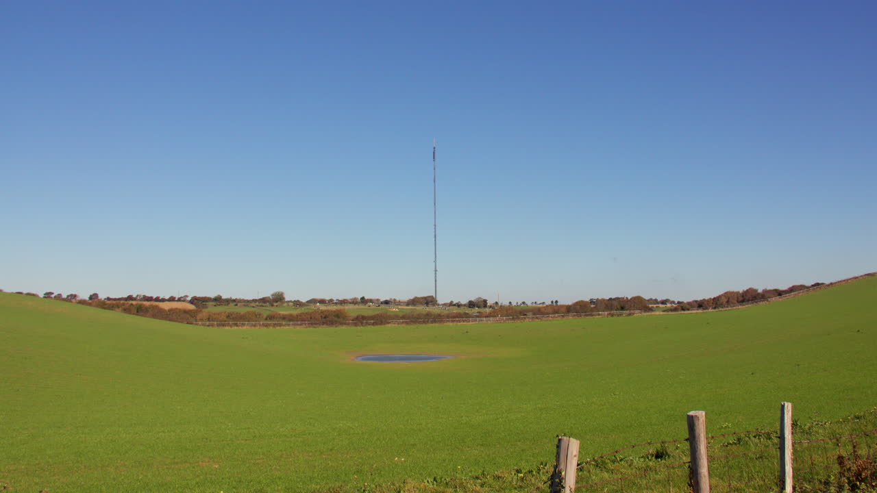 Tall Communication Tower in a Green Rural Landscape with Pond