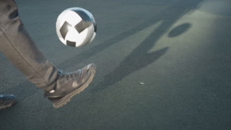 close up of sportsman's legs skillfully kicking soccer ball upwards, capturing dynamic movement and shadow on urban sports arena ground