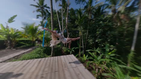 beautiful blond woman spreading her arms and enjoying the swing set in the tropical nature of bali