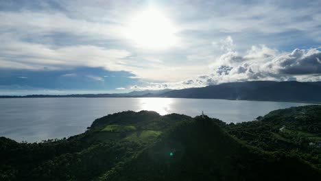 vista aérea de alto contraste de los picos de las montañas de la selva con un faro de bote en la cima que revela un vasto océano y un espectacular paisaje nublado