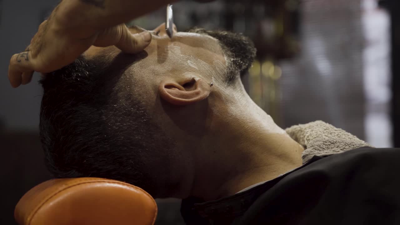 Barber Shaving Male's Cheek With Open Razor - close up