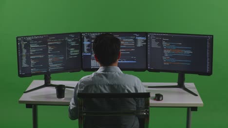 back view of tired asian man developer stretching while write code with multiple computer screens in green screen studio