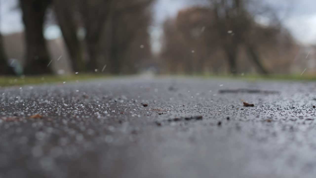 Low-angle close-up of hail bouncing on wet asphalt walkway in autumn weather