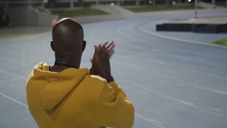 African-american-male-coach-clapping-watching-disabled-male-athlete-with-running-blade-training