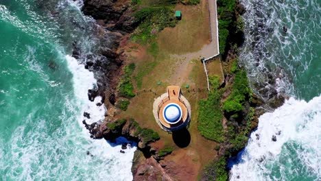 overhead view of structure at tip of rocky seaside peninsula with green ocean waves crashing onshore, puerto plata, dominican republic, above aerial rising