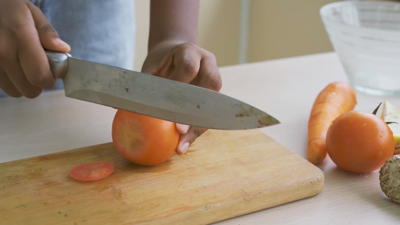 Close up of hand african american girl chopping  tomatoes on cutting board with knife in kitchen