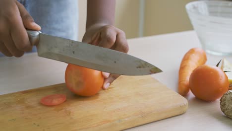 close up of hand african american girl chopping  tomatoes on cutting board with knife in kitchen