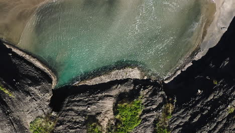 A-shallow-pool-of-translucent-like-water-forms-at-low-tide-on-Piha-Beach,-New-Zealand