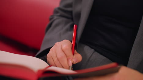 close-up shot of person writing notes in notebook with red pen, business, productivity, and planning concept. focus on hand holding pen and writing, blurred background in modern workspace