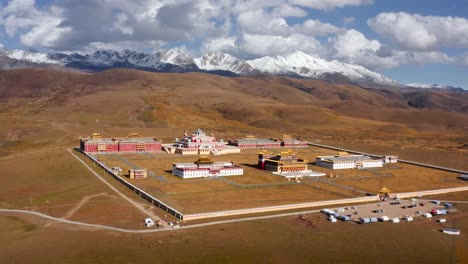 aerial pullback reveals expanse of white mountains and temples in tagong grasslands of sichuan china