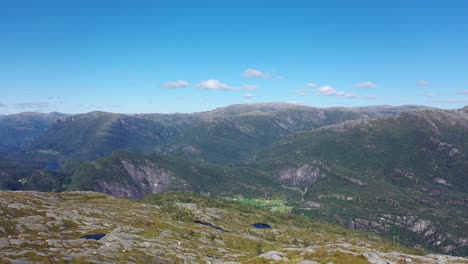 man on mountaintop reaching his achievement and raising his arm to the air to celebrate reaching the top - aerial approaching man and passing with norway mountain landscape in background