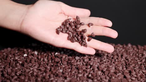 a hand gently sorts chocolate drops on a textured surface under bright lighting, highlighting texture and movement