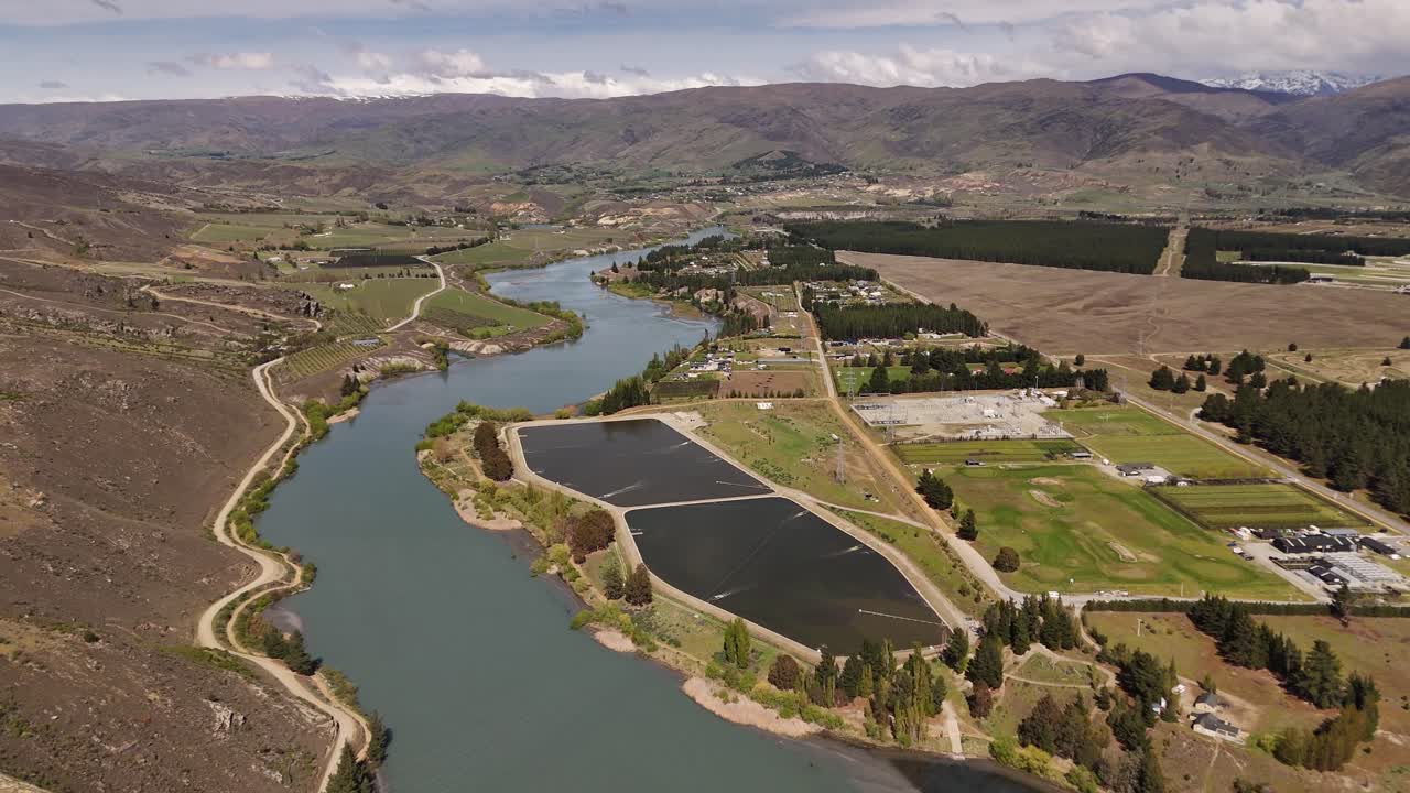 Scenic 4K aerial drone footage of the Clutha River winding past the rural outskirts and infrastructure of Cromwell, New Zealand. Views of oxidation ponds, mountains, and valleys in Otago