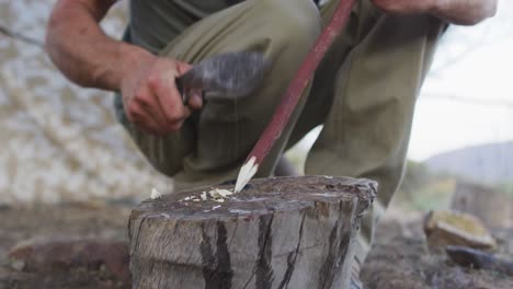 caucasian male survivalist sharpening stick with machete in wilderness