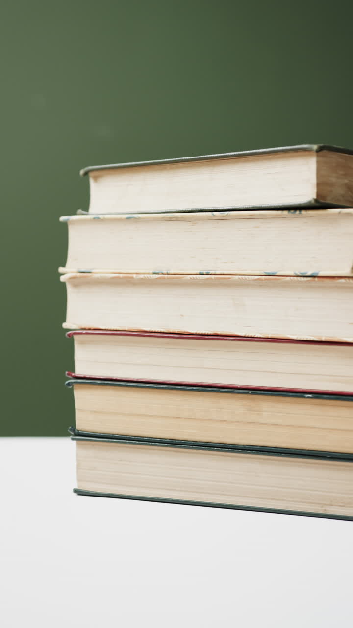 Vertical video of stack of books on green background, in slow motion