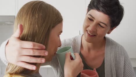 Caucasian-lesbian-couple-embracing-each-other-while-having-coffee-together-in-the-kitchen-at-home