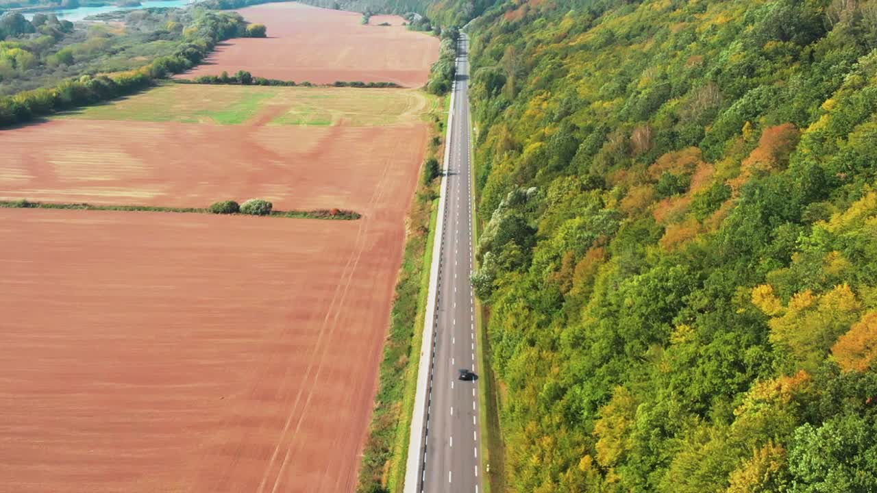 toma aérea del auto recorriendo la carretera en otoño, día soleado con bosque colorido, alejándose