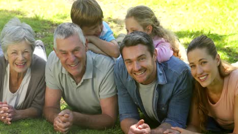 familia de varias generaciones sonriendo y acostada en el suelo en un parque