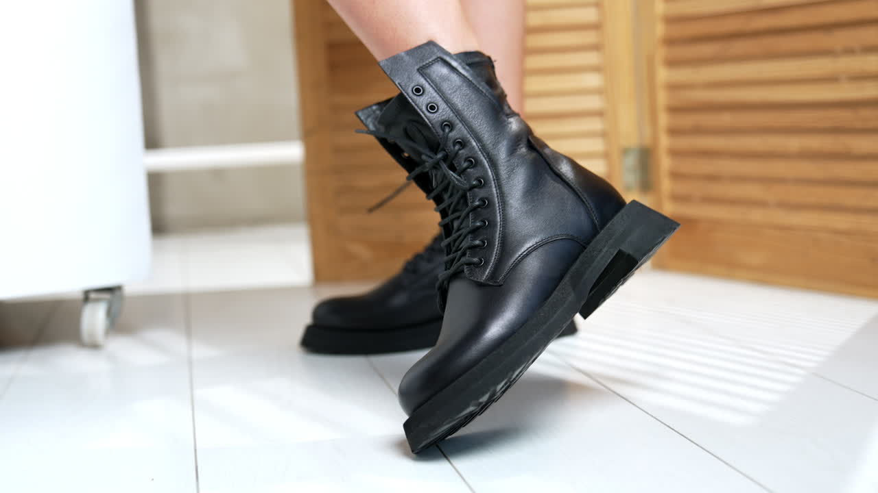 Demonstration of stylish army boots with laces on female feet. Woman moving her feet in fashionable footwear in front of camera. Close up. Wooden screen at backdrop.