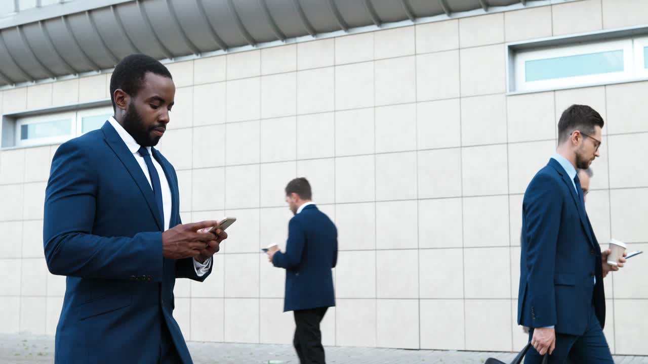 African American young businessman walking down street and using smartphone
