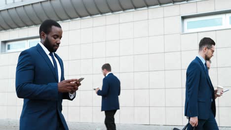 african american young businessman walking down street and using smartphone