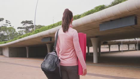 Caucasian-woman-walking-under-bridge-with-yoga-mat