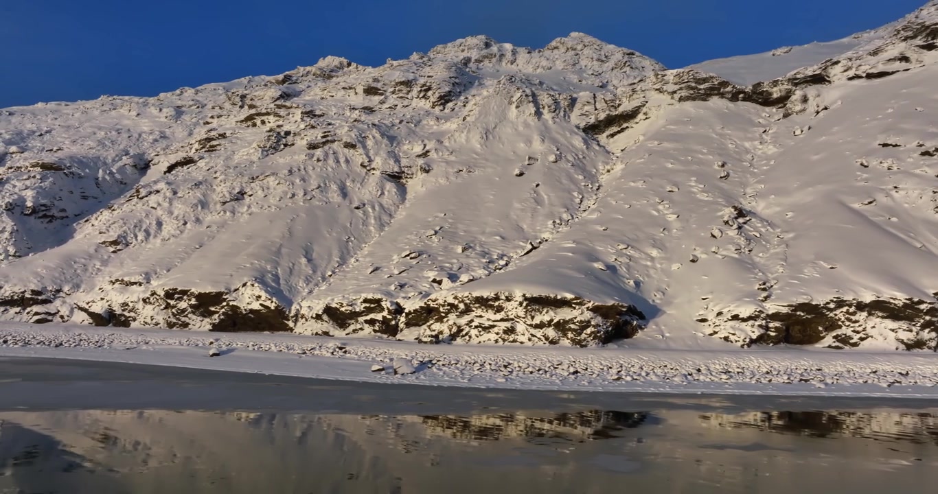 Scogliere innevate illuminate dal sole si ergono sopra la costa ghiacciata di Kleifarvatn in Islanda, con acqua scura e riflettente e una ruvida texture vulcanica in un aspro paesaggio invernale.