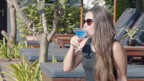 close shot of a young lady relaxing by the pool drinking a cocktail in the hotel grounds