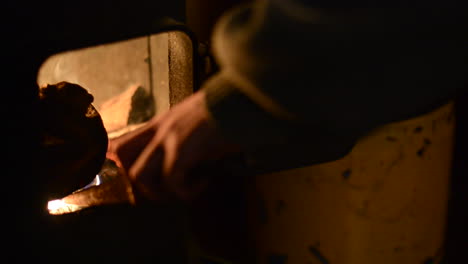 man placing a piece of sharpened wood inside a stove