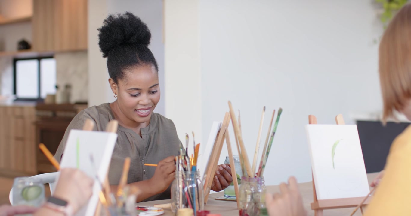 African woman in olive top preparing paint, painting green stroke in group session at kitchen