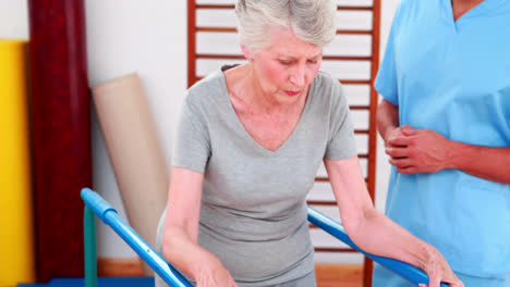 Physical-therapist-watching-patient-walk-with-parallel-bars