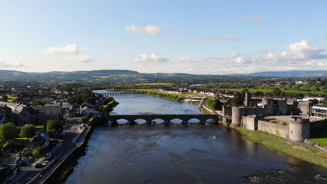 Aerial-View-of-Limerick-City,-Ireland,-Revealing-View-of-Shannon-River-Riverside-With-King-John's-Castle-and-Residential-Neighborhood,-Pull-Back-Drone-Shot